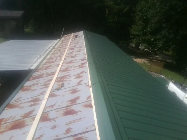 Old rusted panels beside newly installed green metal roofing — Wind Damage Roof Repair by Roofing Brothers in Smithfield
