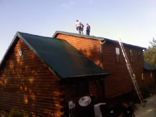 Crew on the ridge of a green metal roof on a two story log home in Smithfield