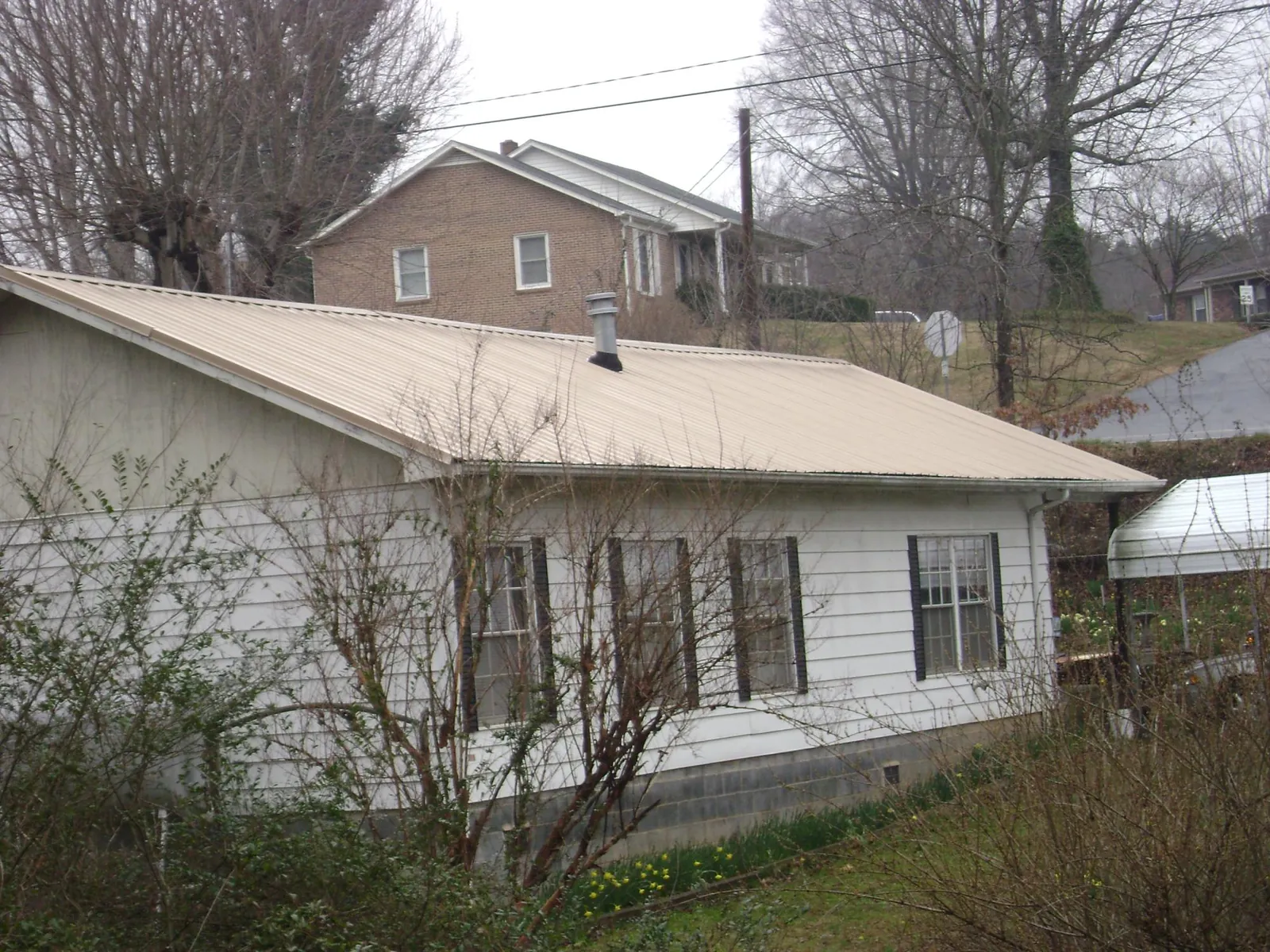 Tan metal roof on a white sided house set into a hillside — Commercial Roofing by Roofing Brothers in Smithfield